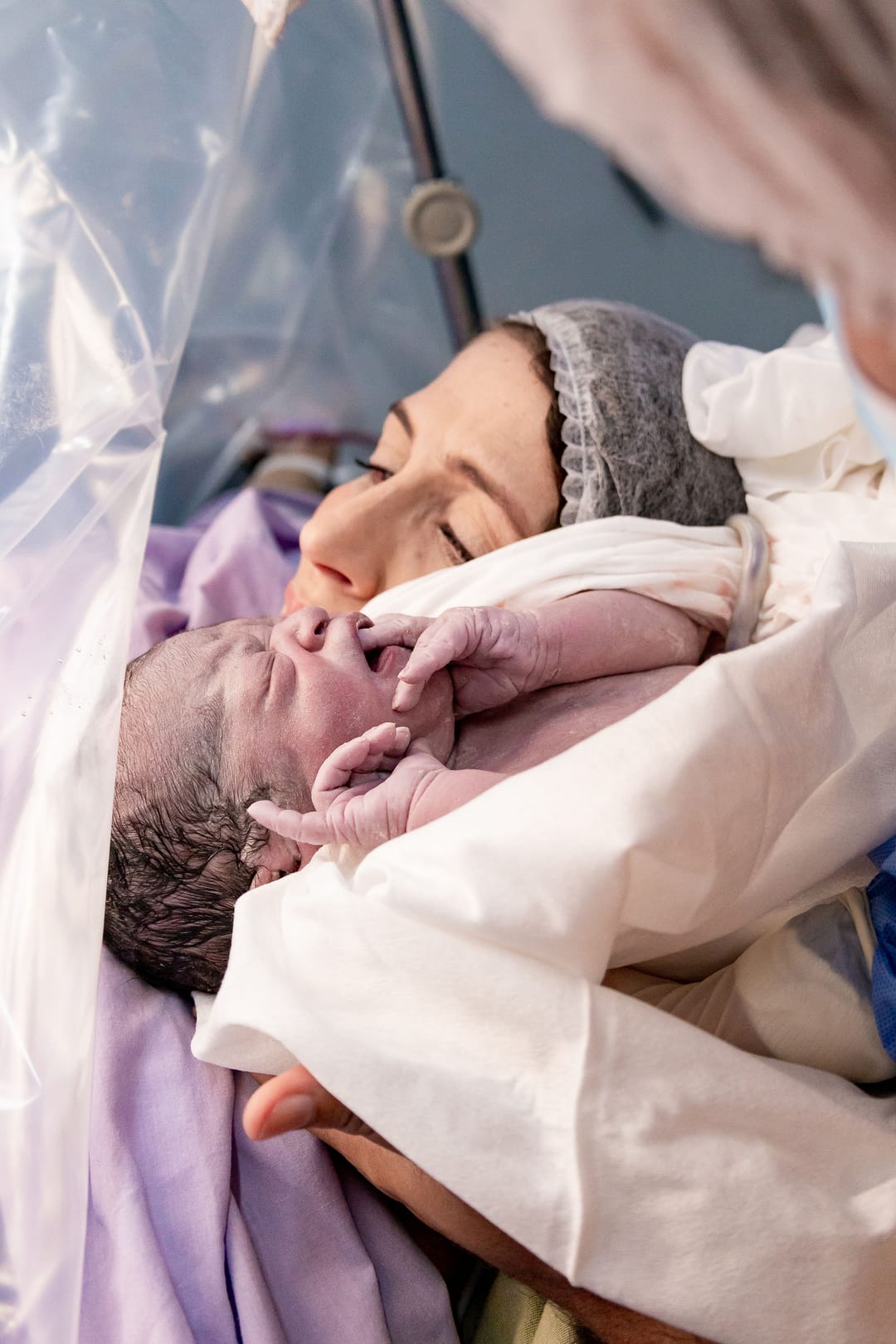 O bebê no rosto da mãe, com as mãozinhas na boca, e a cortina como moldura.
