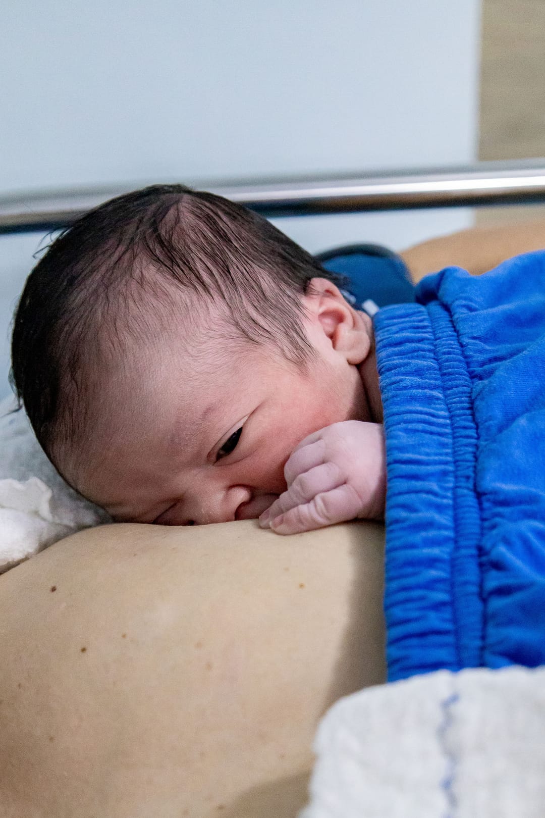Na recuperação, o bebê no peito da mãe, de olho aberto e punho na boca.