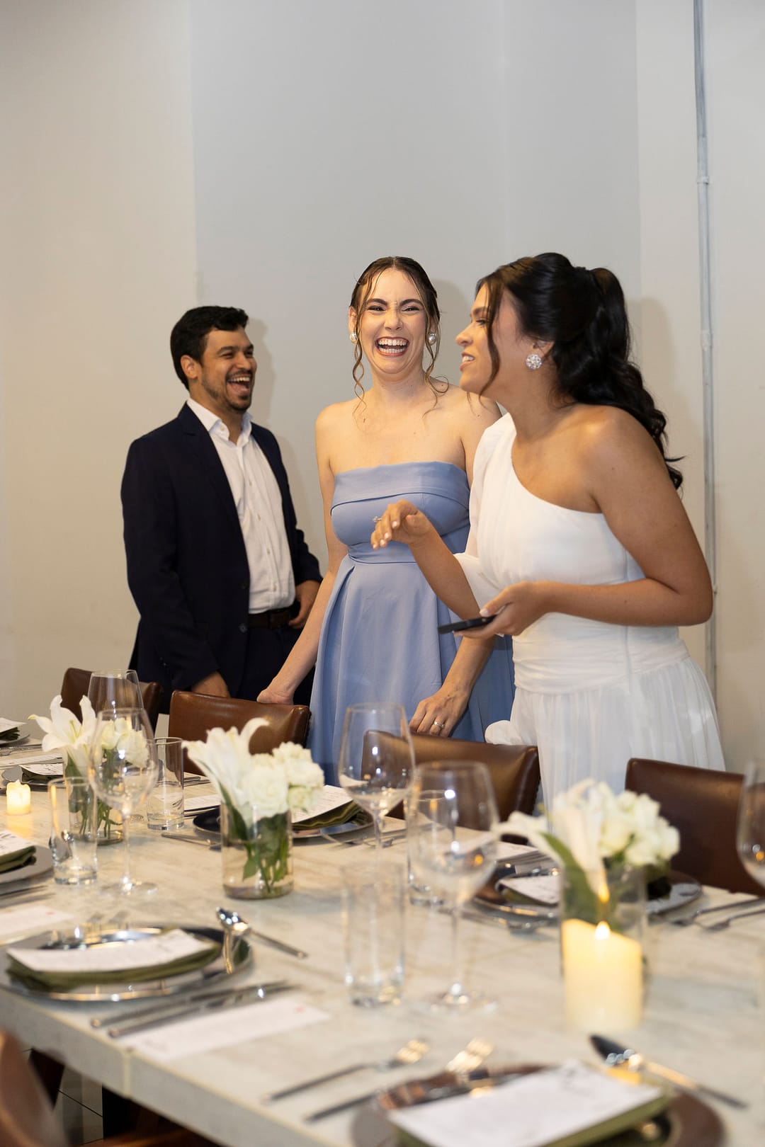 A noiva ri com duas amigas ao lado da mesa posta à luz de velas.