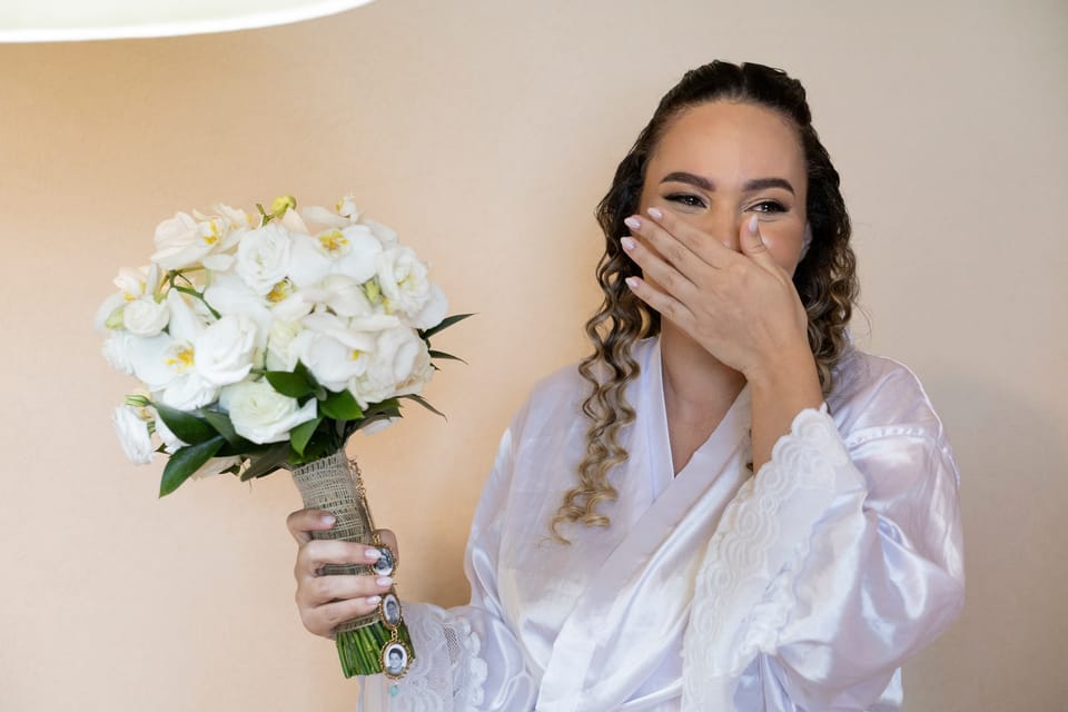Ao receber o buquê de orquídeas, a noiva cobre a boca, com os olhos marejados.