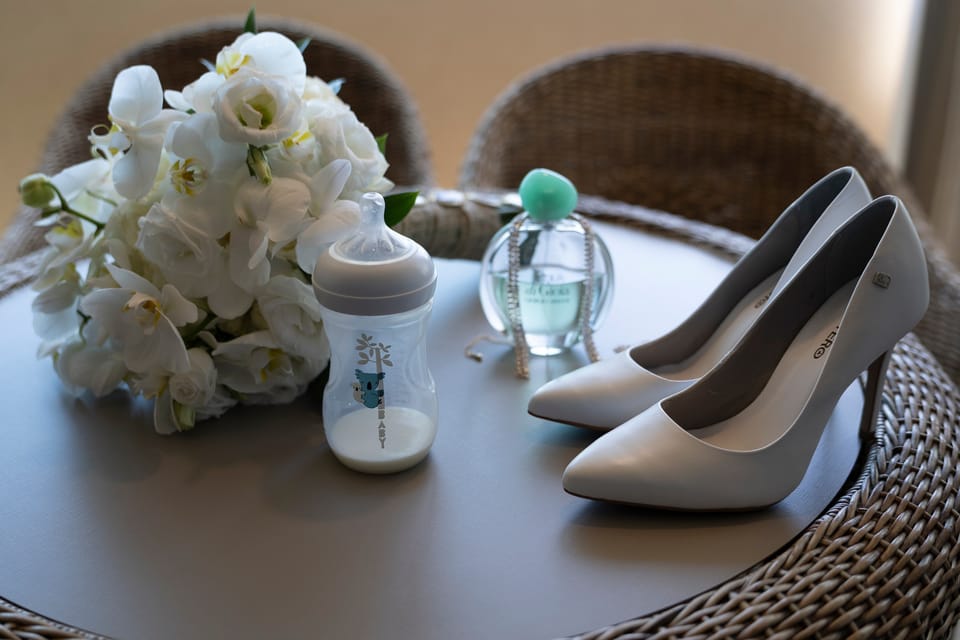 Na mesa de palha, o buquê, os sapatos, o perfume e a mamadeira do bebê.