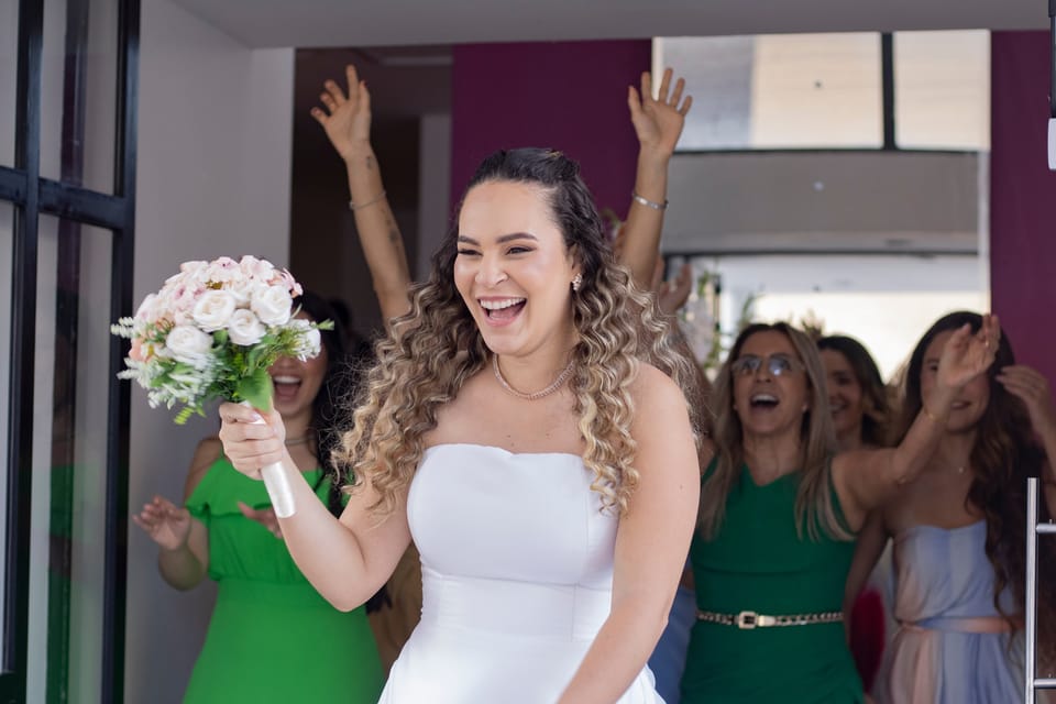 A noiva sai para jogar o buquê, gargalhando, e as amigas vibram de braços para cima.