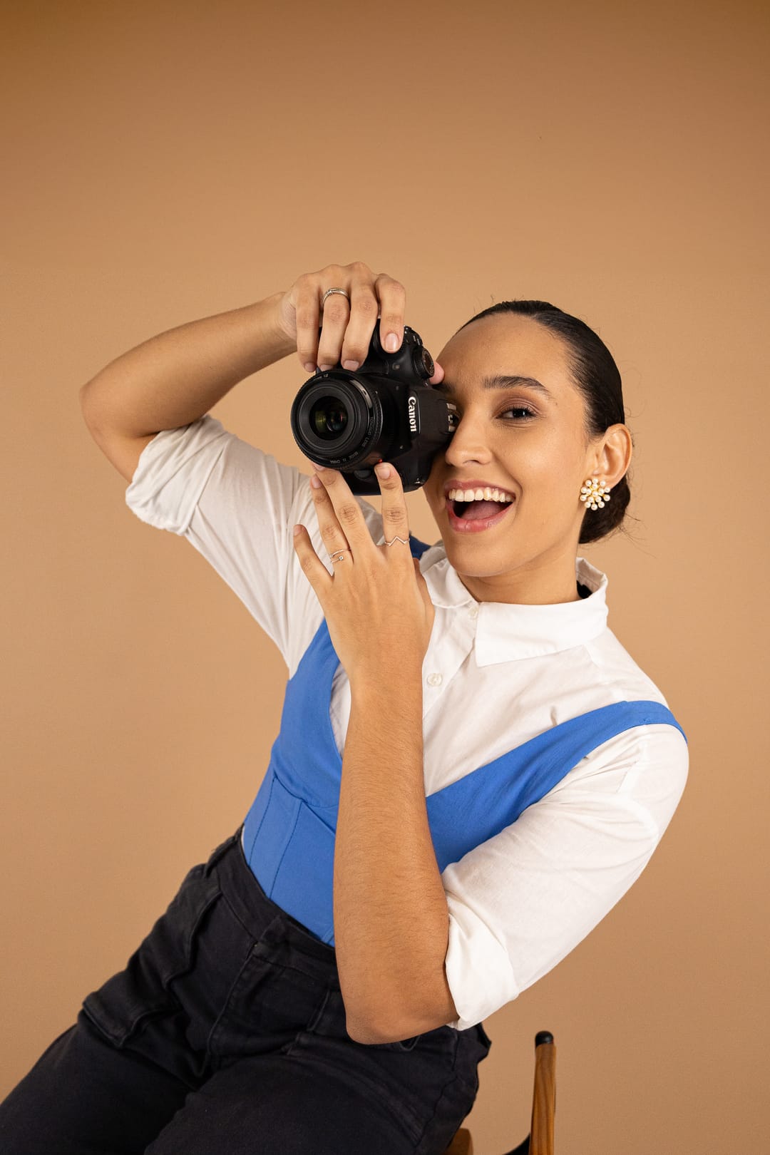 A Marcela ri com a câmera no olho, diante de um fundo caramelo.