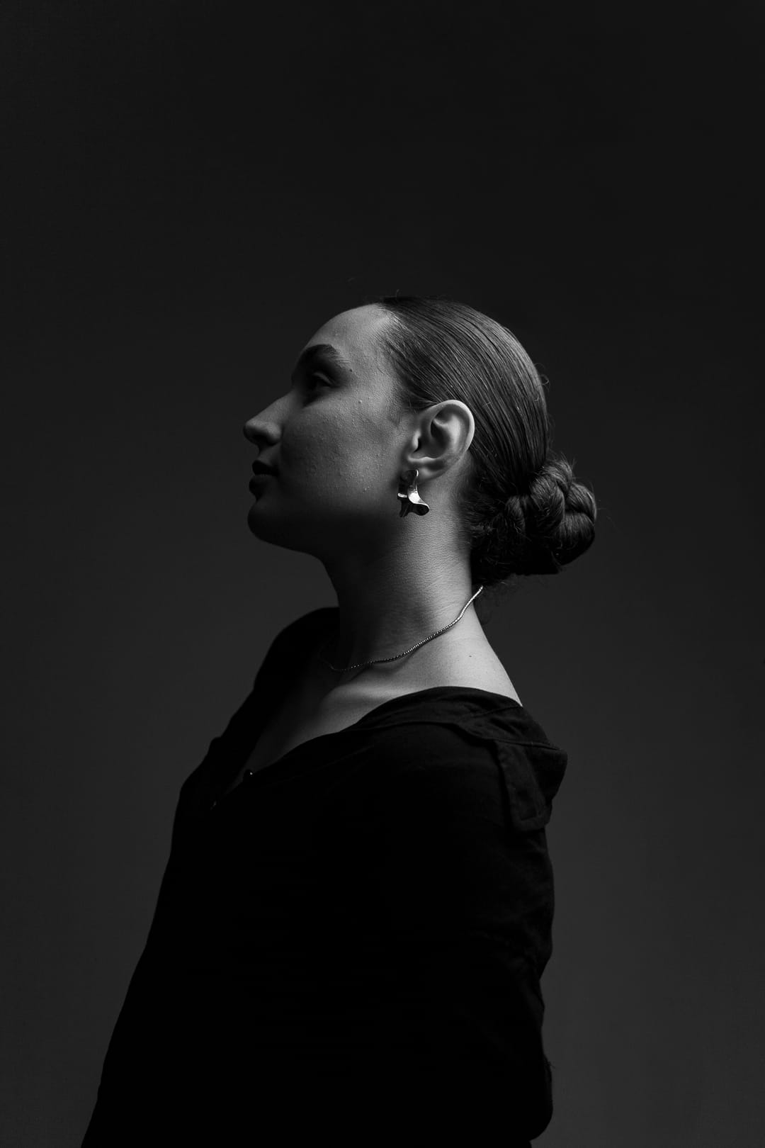 A Marcela de perfil, em preto e branco, olhando para cima, com o cabelo preso e um brinco de pétala.