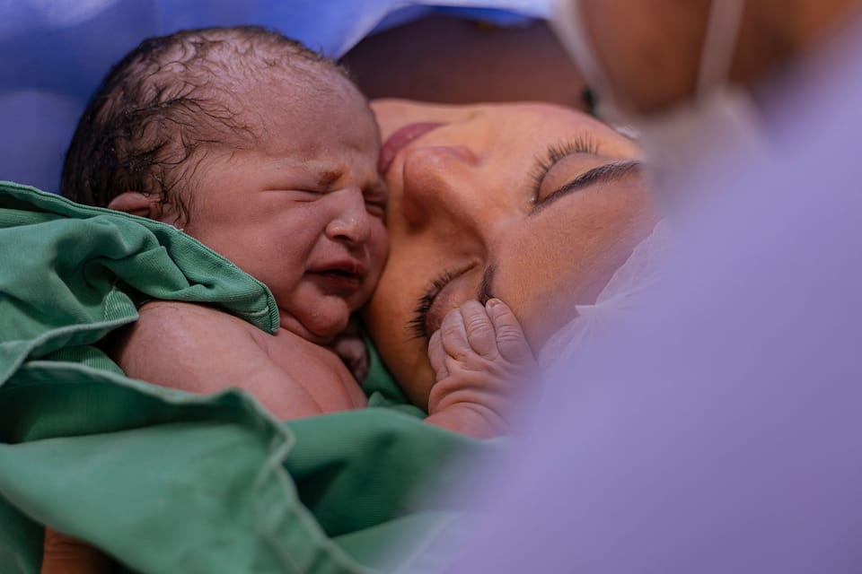 O recém-nascido chora rosto com rosto com a mãe, enrolado no pano verde.