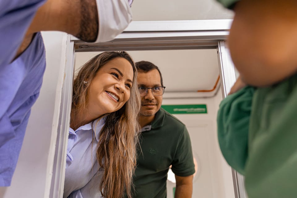 Dois familiares espiam pela porta para ver o bebê; ela sorri de orelha a orelha.