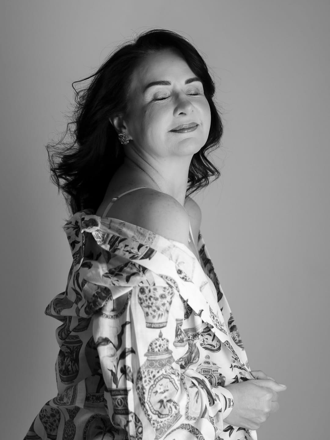 Em preto e branco, uma mulher de olhos fechados, serena, de blusa estampada.