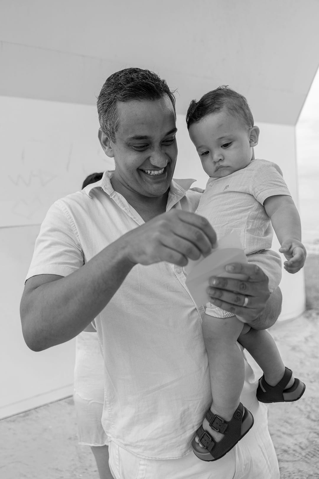 O pai, com o filho no colo, abre um envelope e sorri.