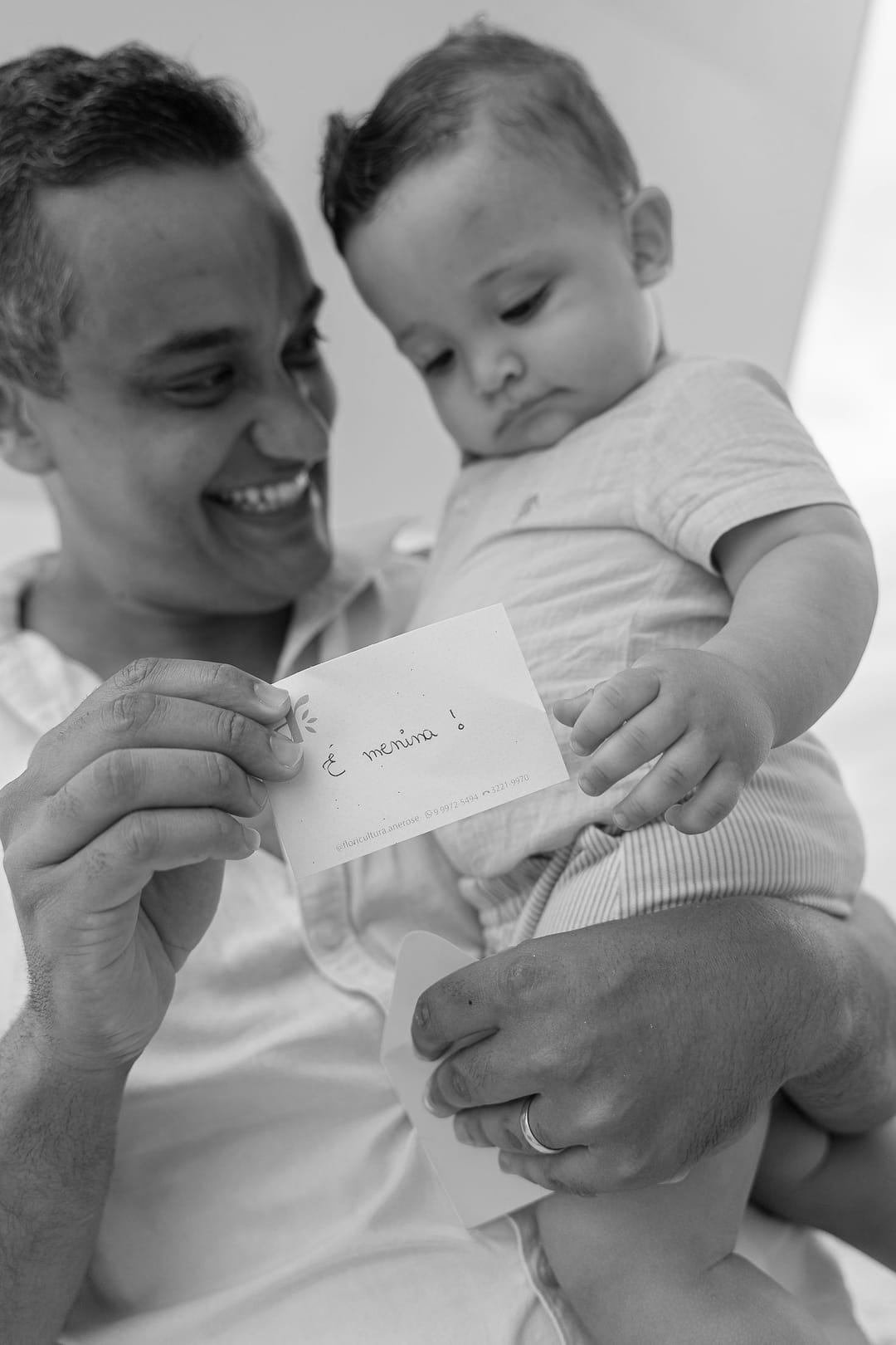 O pai sorri ao ler o cartão com a resposta, e o filho estica a mão para pegá-lo.