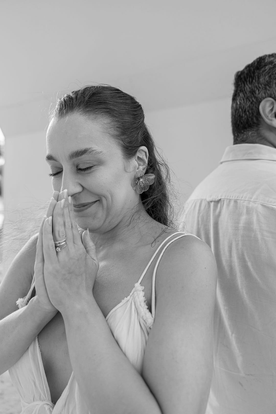 De mãos juntas diante do rosto, a mãe espera de olhos fechados, sorrindo.