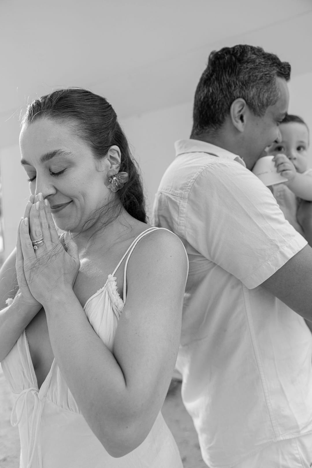 Ela, de olhos fechados e mãos em prece; atrás dela, pai e filho seguram o cartão.