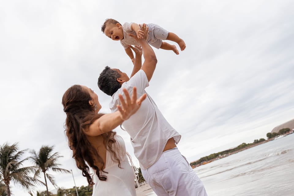 O pai lança o filho para o céu, e a mãe abre os braços, entre coqueiros e o mar.