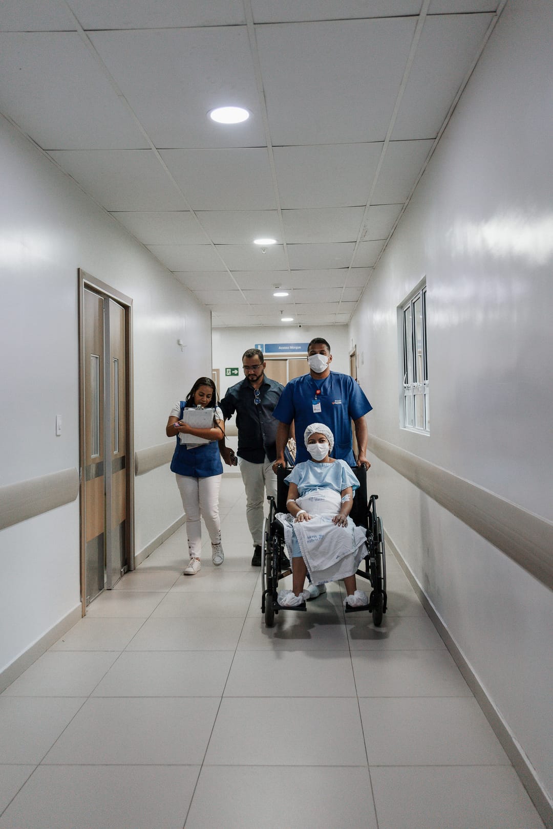 No corredor do hospital, a mãe, com o bebê no colo, vai na cadeira de rodas, acompanhada da família.
